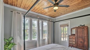 Une chambre à coucher avec un lit, un ventilateur de plafond, une commode en bois et une fenêtre avec des rideaux.