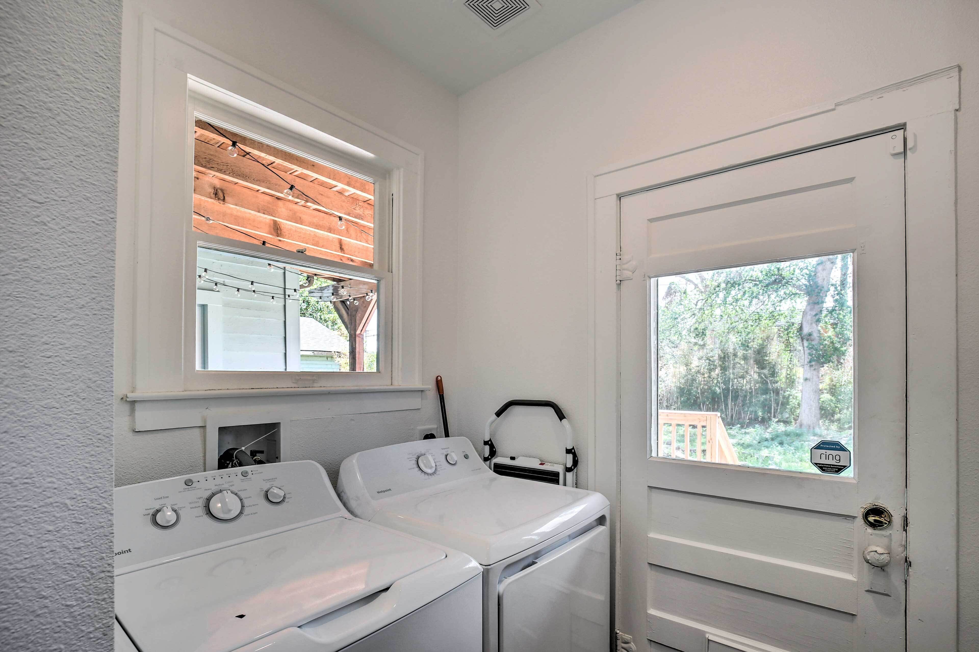 Un cuarto de lavado con dos lavadoras y secadoras blancas, una ventana con vista a una terraza de madera, y una puerta que da a un bosque.