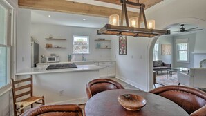Une cuisine moderne avec des meubles blancs, un îlot central et un plafond en bois. On y trouve un coin repas avec des chaises en cuir et une table, ainsi qu’un salon doté d’une cheminée et de sièges confortables.