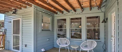 Une véranda couverte avec des poutres en bois et des guirlandes lumineuses, deux fauteuils en osier blancs et une petite table.