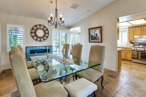 A dining area with a glass-top table, wicker chairs, a wall clock, and a chandelier. - Indian Wells Oasis w/ Pool: Walk to Tennis Garden! (Indian Wells)