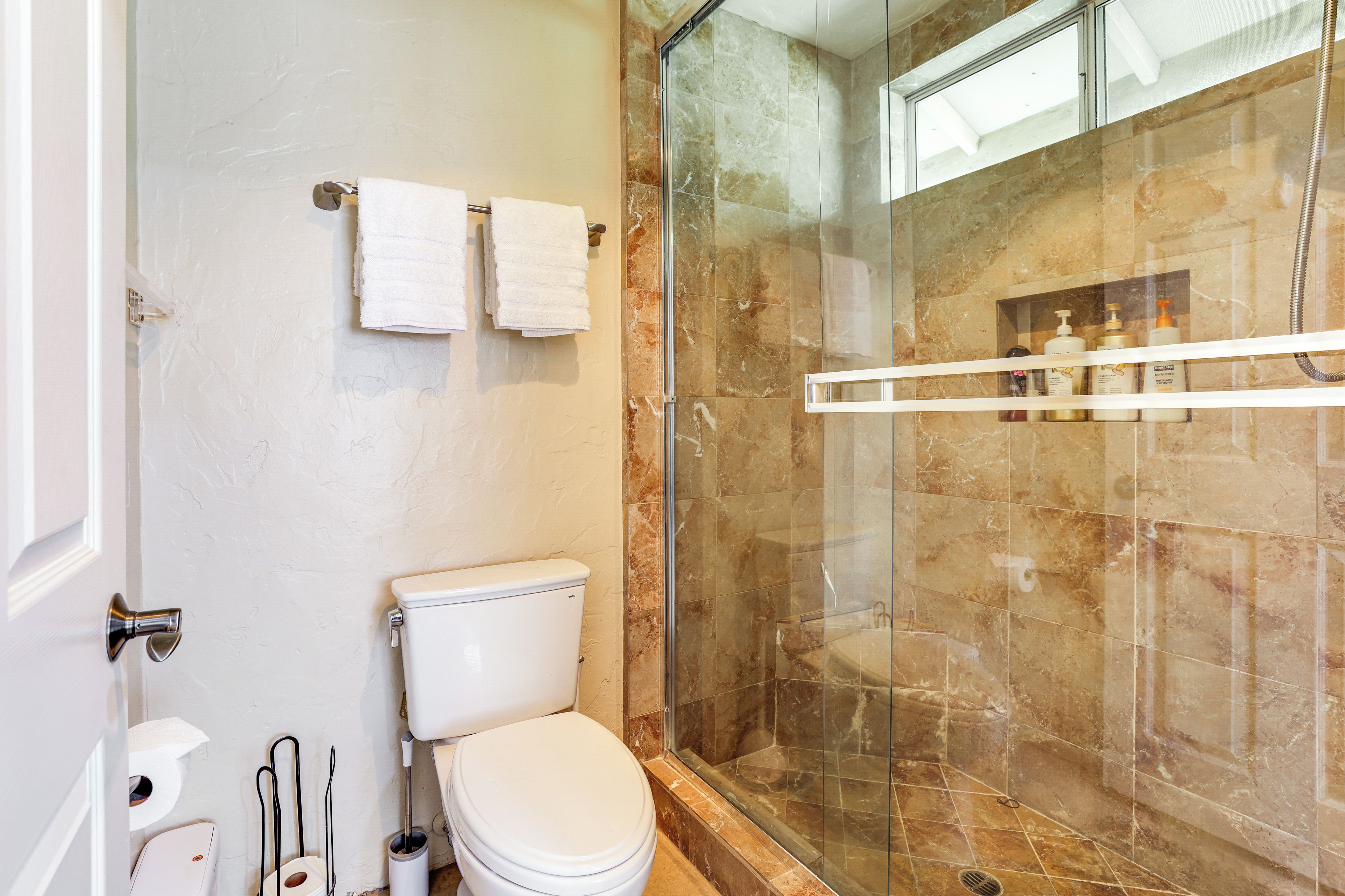 A bathroom with a toilet, a glass-enclosed shower, and a towel rack with two towels.