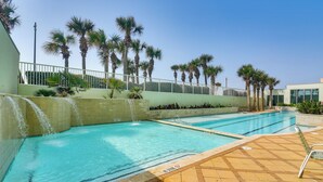Ein Swimmingpool mit Wasserfall, umgeben von Palmen und einem weißen Zaun.