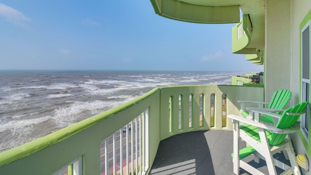 Ein Balkon mit Blick auf das Meer, ein grüner Stuhl und ein kleiner Tisch.