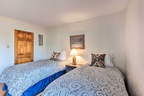 A room with two beds, a wooden door, a wall-mounted picture, and a bedside lamp. - El Prado Townhome w/ View of Taos Mountains! (El Prado)