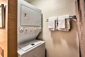 A compact laundry area with a front-loading washer and dryer, a towel rack with folded towels, and a plain wall. - El Prado Townhome w/ View of Taos Mountains! (El Prado)