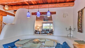 A rustic interior with a wooden ceiling, a round table with blue and beige placemats, and a view of a living area through a window. - El Prado Townhome w/ View of Taos Mountains! (El Prado)
