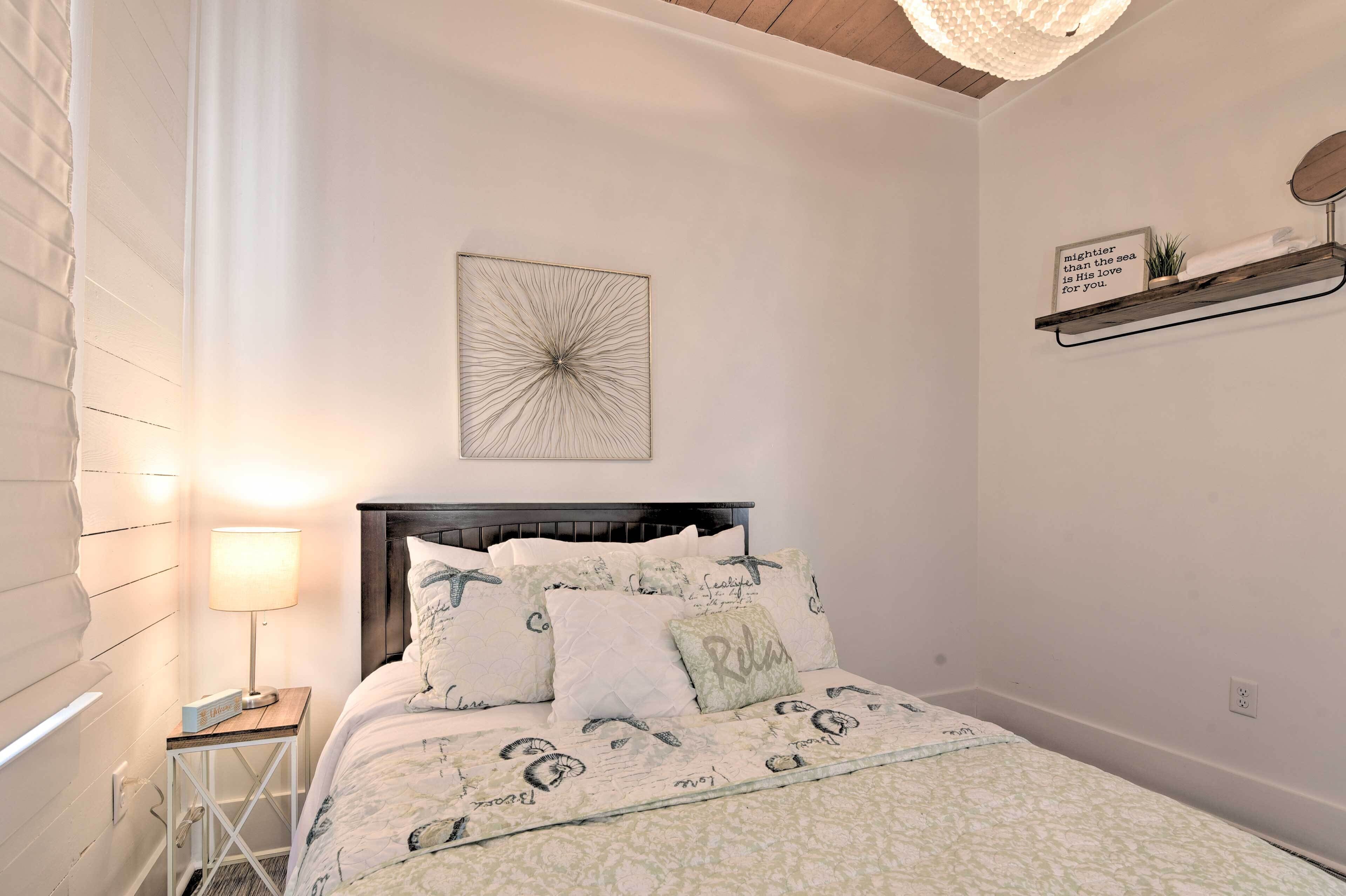 A bedroom with a bed, a bedside table, a lamp, a wall art piece, and a shelf with a decorative item.