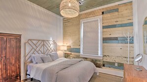 A bedroom with a wooden headboard, a large bed, a wooden wardrobe, a hanging light fixture, and a window with blinds. - Near Beach & Strand: Bright Cottage in Galveston (Galveston)