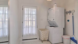 A laundry room with a washing machine, a drying machine, a small trash bin, and a broom. - Near Beach & Strand: Bright Cottage in Galveston (Galveston)