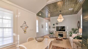 A dining area with a table and chairs, a chandelier, and a television in the background. - Near Beach & Strand: Bright Cottage in Galveston (Galveston)