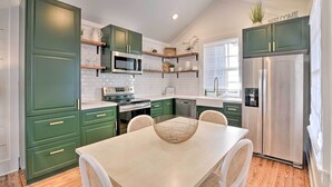 A modern kitchen with green cabinets, stainless steel appliances, and a dining area with a light-colored table and wicker chairs. - Near Beach & Strand: Bright Cottage in Galveston (Galveston)