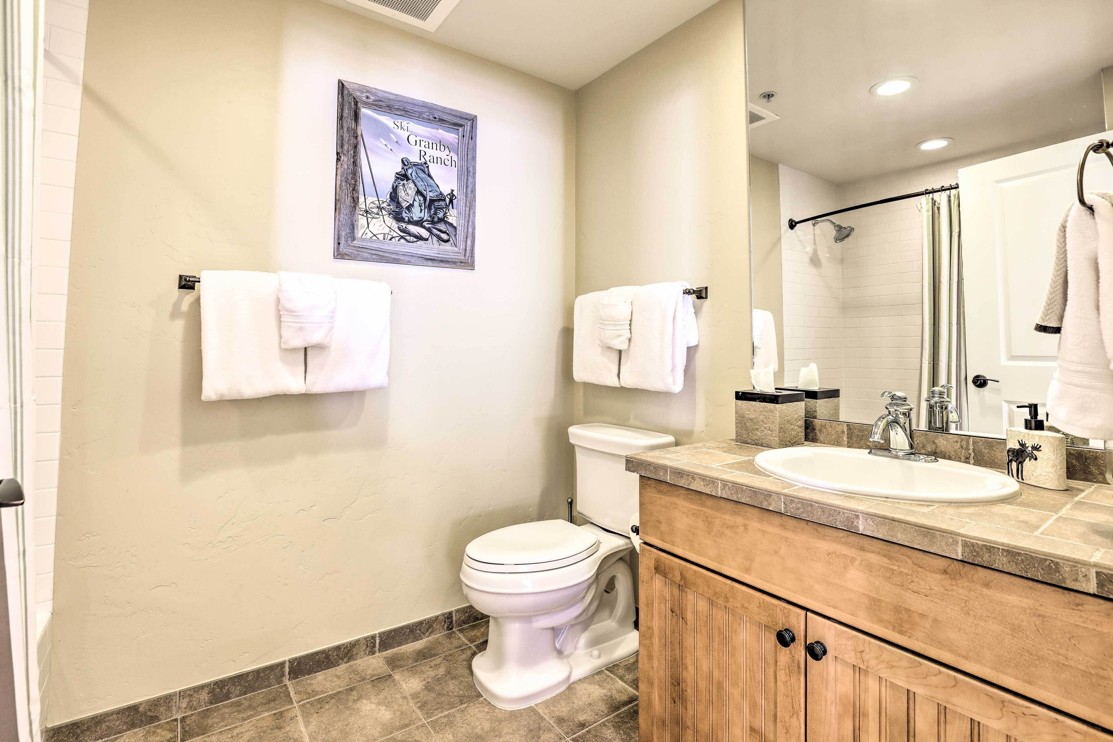 A bathroom with a toilet, sink, and mirror. There are towels hanging on the wall and a framed picture above the toilet.