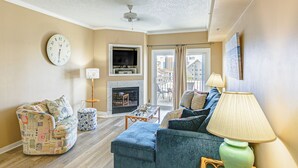 A living room with a sofa, ottoman, and a television. There is a fireplace and a window with curtains. - Steps to Sand! Family-friendly Ocean City Getaway (Ocean City)