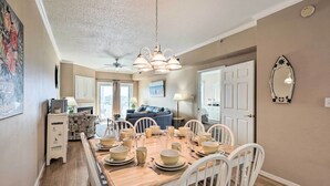 A dining area with a wooden table set for six, white chairs, and a chandelier. - Steps to Sand! Family-friendly Ocean City Getaway (Ocean City)