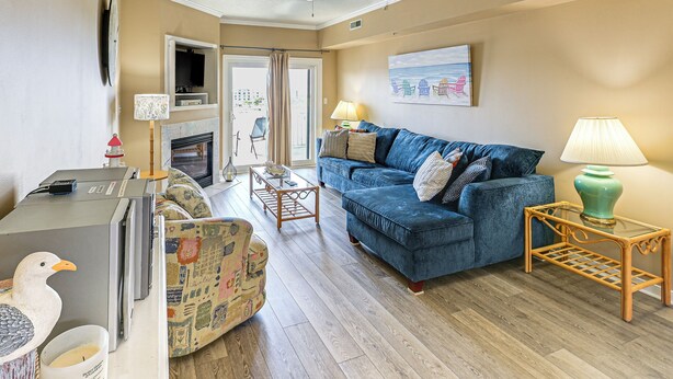 A living room with a blue sofa, a wooden coffee table, a patterned armchair, and a small table with a lamp. - Steps to Sand! Family-friendly Ocean City Getaway (Ocean City)