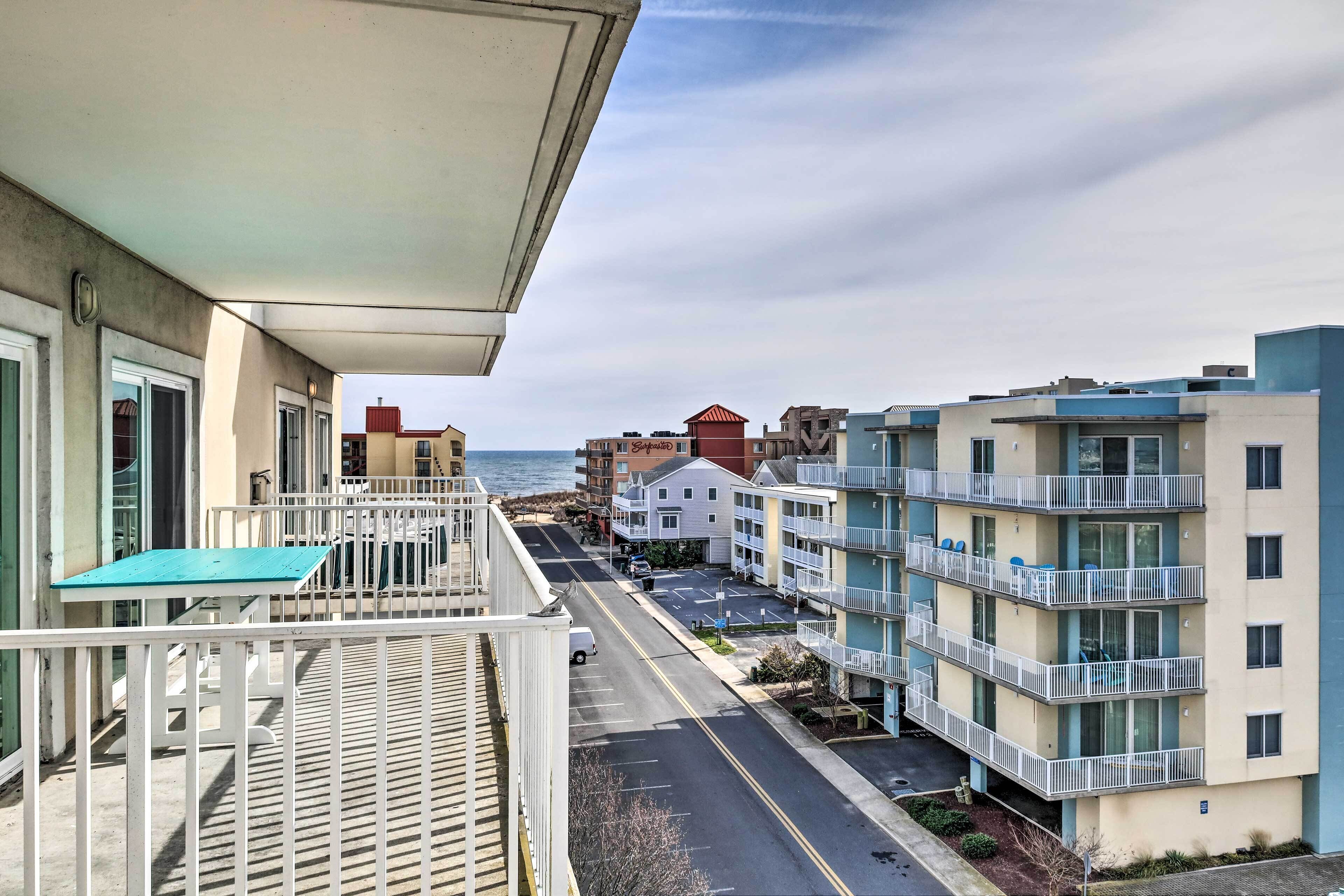 A residential building with balconies, a street in front, and a view of the ocean.