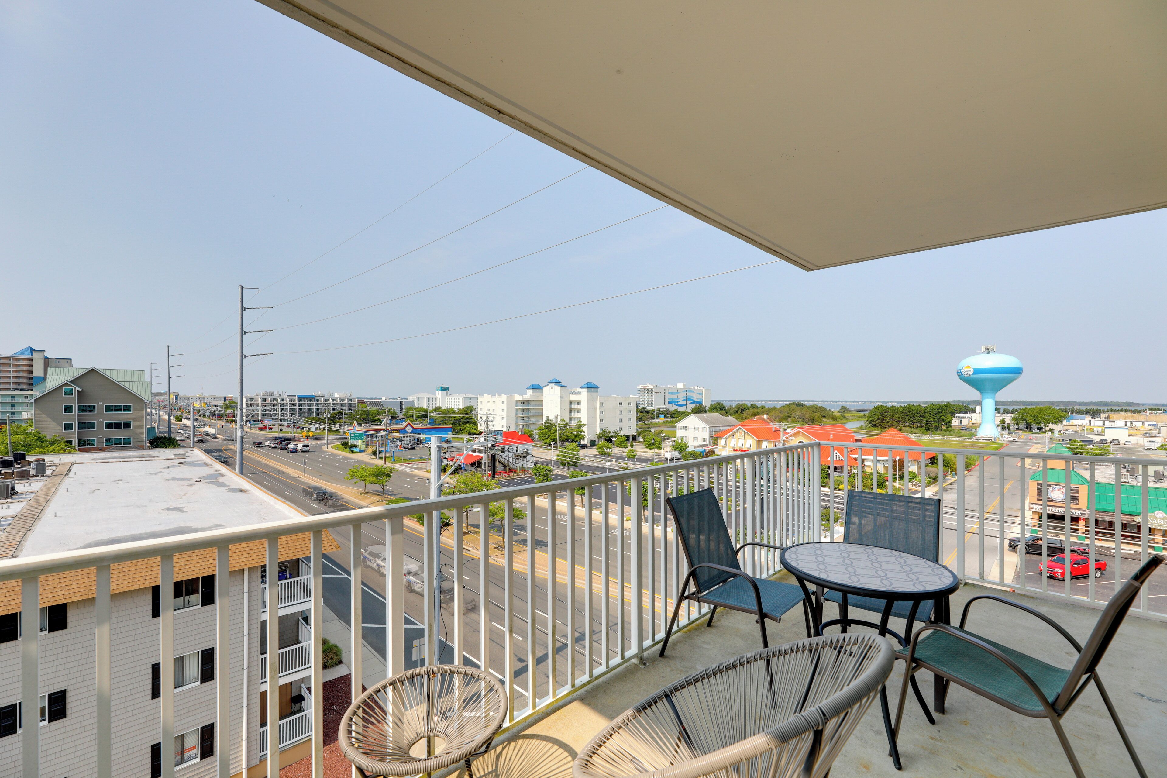 Ein Balkon mit Korbstühlen und einem Tisch, mit Blick auf eine Stadtlandschaft mit Gebäuden und einem Wasserturm.