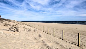 A sandy beach with a wooden fence and a building in the background. - Steps to Sand! Family-friendly Ocean City Getaway (Ocean City)