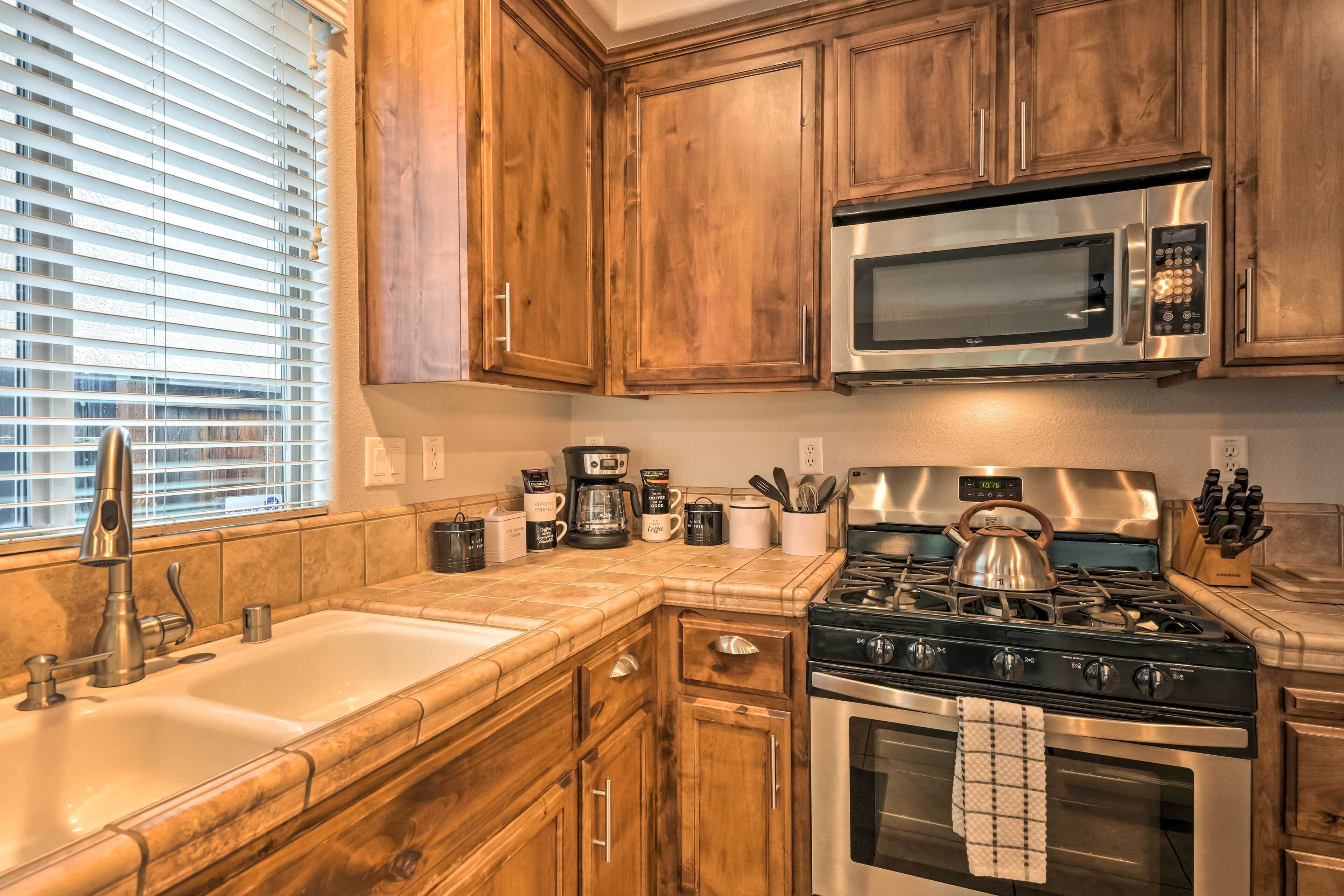 A kitchen with wooden cabinets, a stainless steel microwave, a gas stove, and a sink.
