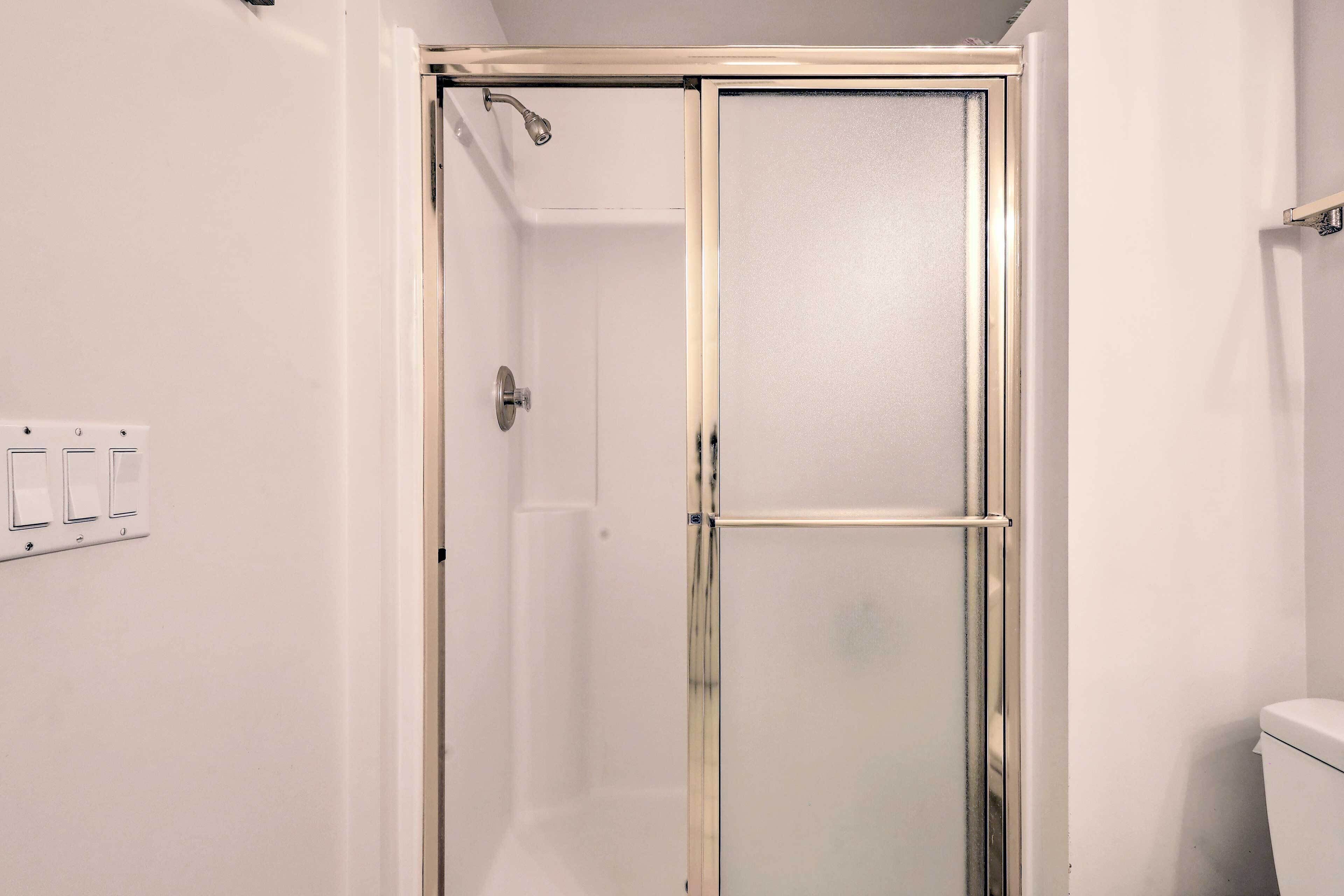 A walk-in shower with a glass door, a white toilet, and a wall-mounted light switch.