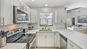 A modern kitchen with white cabinets, a built-in oven, a sink, and a window with blinds. - Port Orange Oasis: Close to Beaches & Dining! (Port Orange)