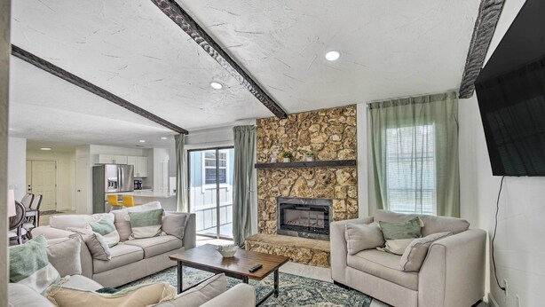 A living room with a stone fireplace, beige sofas, and a coffee table. - Port Orange Oasis: Close to Beaches & Dining! (Port Orange)