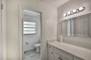A bathroom with a toilet, a sink with a mirror, and a vanity with drawers. - Port Orange Oasis: Close to Beaches & Dining! (Port Orange)