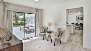 A spacious room with a large sliding glass door leading to an outdoor patio, a small round table with a lamp, two armchairs with patterned cushions, and a wooden bench. - Port Orange Oasis: Close to Beaches & Dining! (Port Orange)