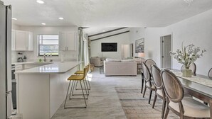 A modern kitchen with a central island, a dining area with a long table and chairs, and a living room with a sofa and a TV. - Port Orange Oasis: Close to Beaches & Dining! (Port Orange)