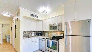 A modern kitchen with white cabinets, stainless steel appliances, and a tiled backsplash. - Walk to Galveston Beach: Resort Condo w/ Perks! (Galveston)