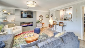 A modern living room with a fireplace, seating area, and a kitchen visible through an open doorway.