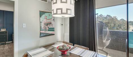 Un comedor con una mesa preparada para cuatro personas, una lámpara colgante y vistas al exterior a través de un ventanal.