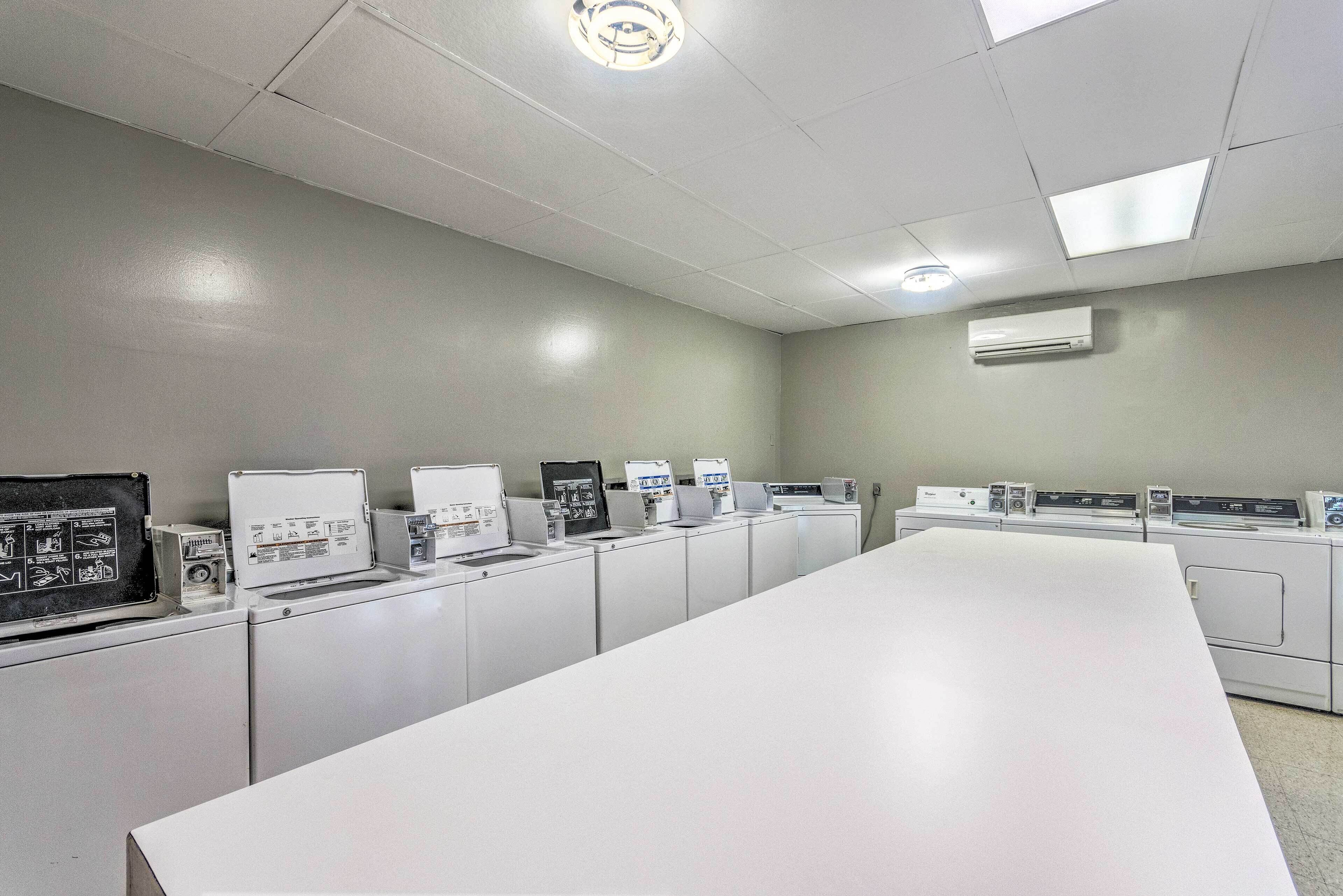 Een wasserette met meerdere wasmachines en drogers, een grote witte tafel en een plafond met fluorescentielampen en een airconditioning.
