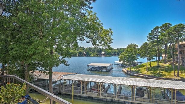 A lakeside view with docked boats, a covered seating area, and a distant building.
