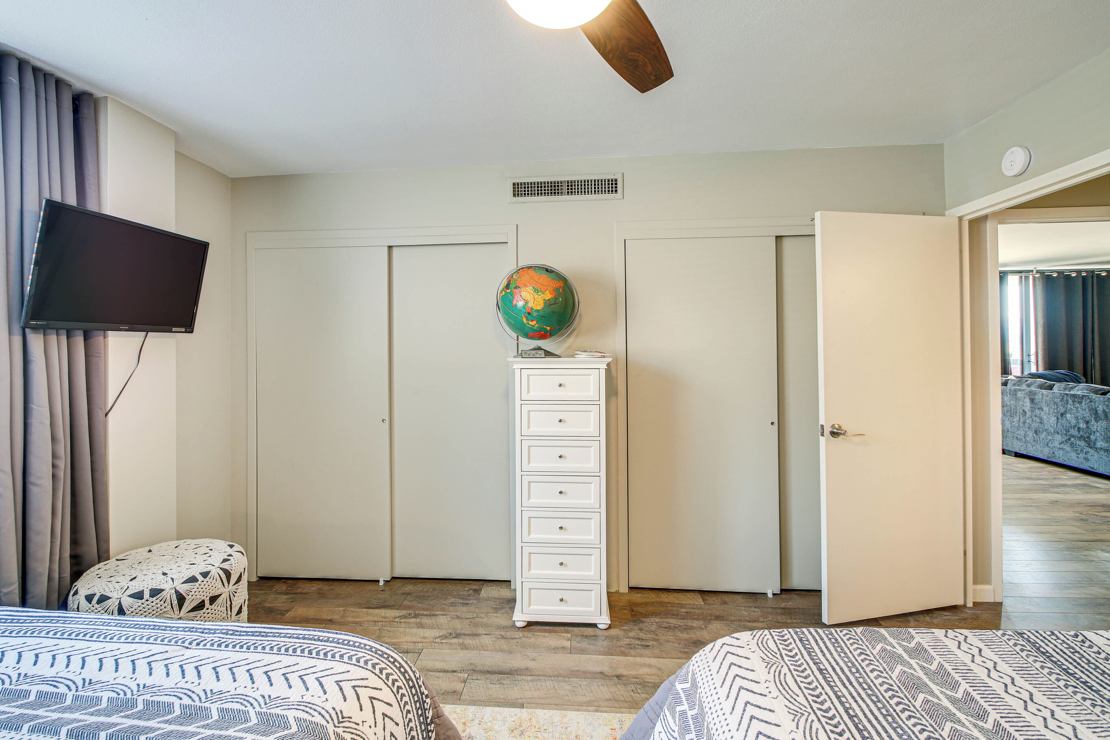 A bedroom with two beds, a flat-screen TV, a globe, and a white dresser.