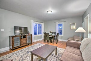 Uma sala de estar com televisão, um aparador de madeira, mesa de jantar, cadeiras e um sofá.