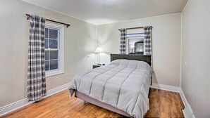 Une chambre à coucher avec un lit, une table de chevet, une lampe et une fenêtre avec des rideaux.