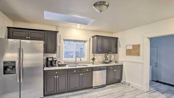 A modern kitchen with dark cabinets, stainless steel appliances, a skylight, and a window.