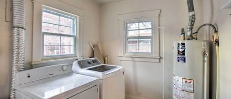 A laundry room with a front-loading washer and dryer, two windows, a water heater, and a vent pipe.