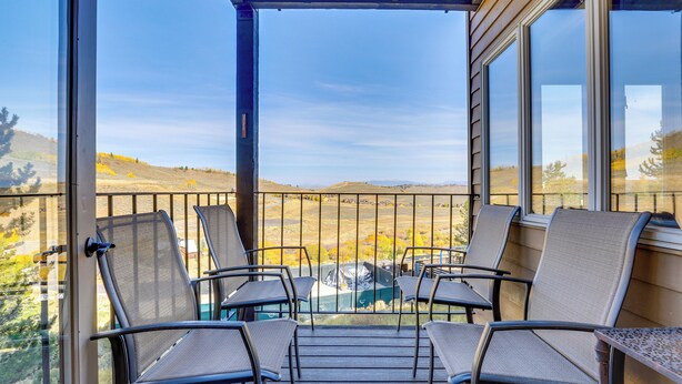 A balcony with four chairs and a table, overlooking a scenic landscape with hills and trees.