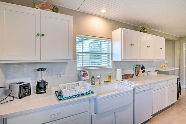 A modern kitchen with white cabinets, a built-in dishwasher, a toaster, a blender, and a window with blinds.