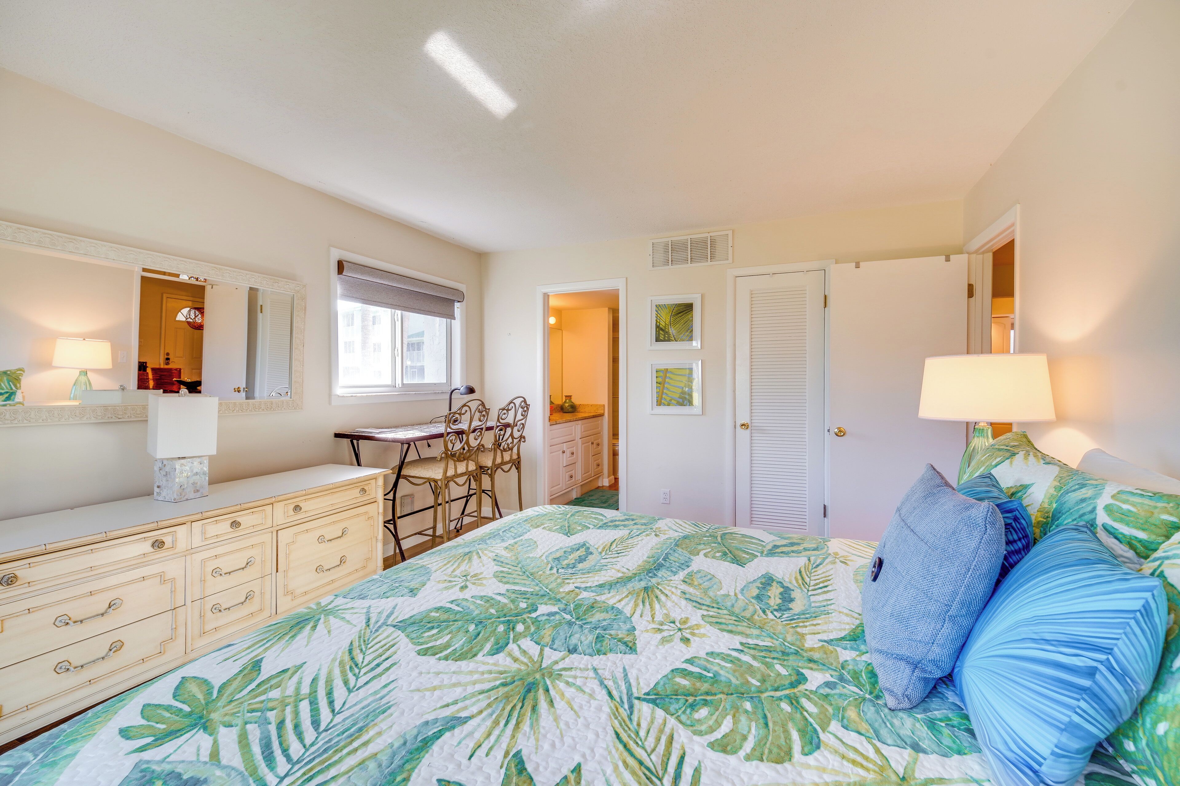 A bedroom with a bed, a desk, and a chair. There is a dresser and a door leading to another room.