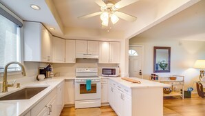 Une cuisine moderne avec des armoires blanches, un four encastré, un four à micro-ondes et un ventilateur de plafond.