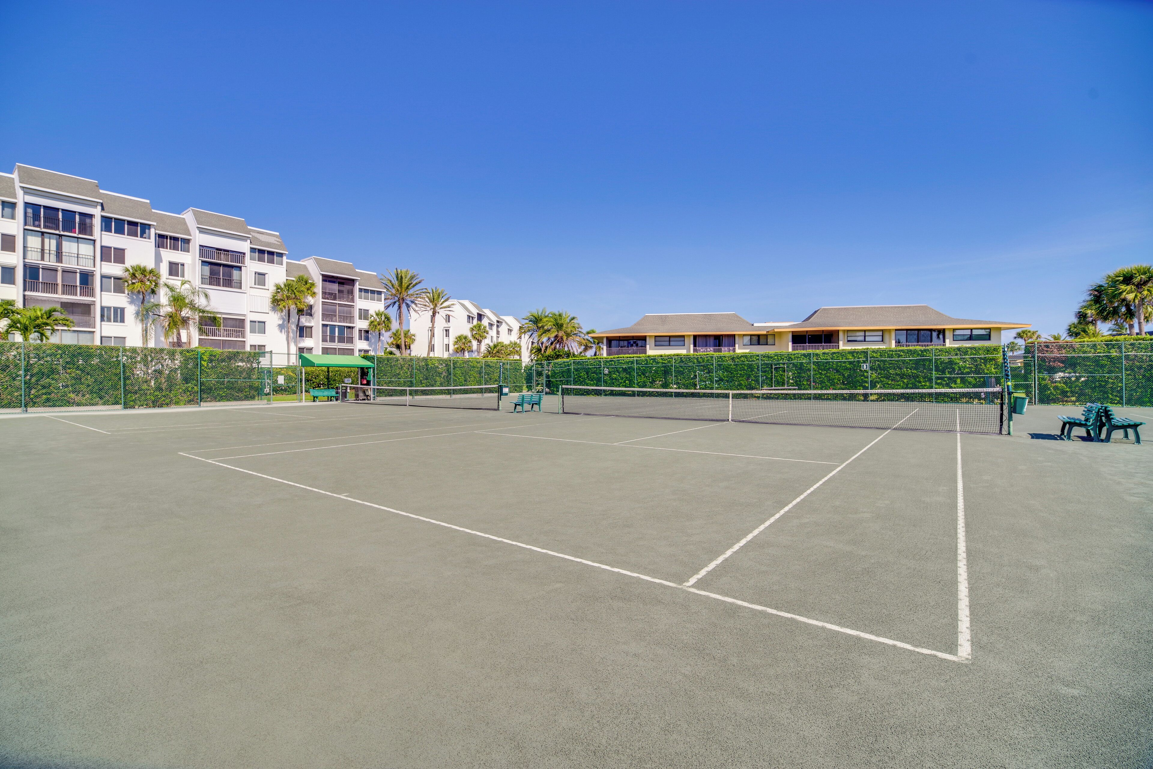 An outdoor tennis court with a net, surrounded by a fence and benches.