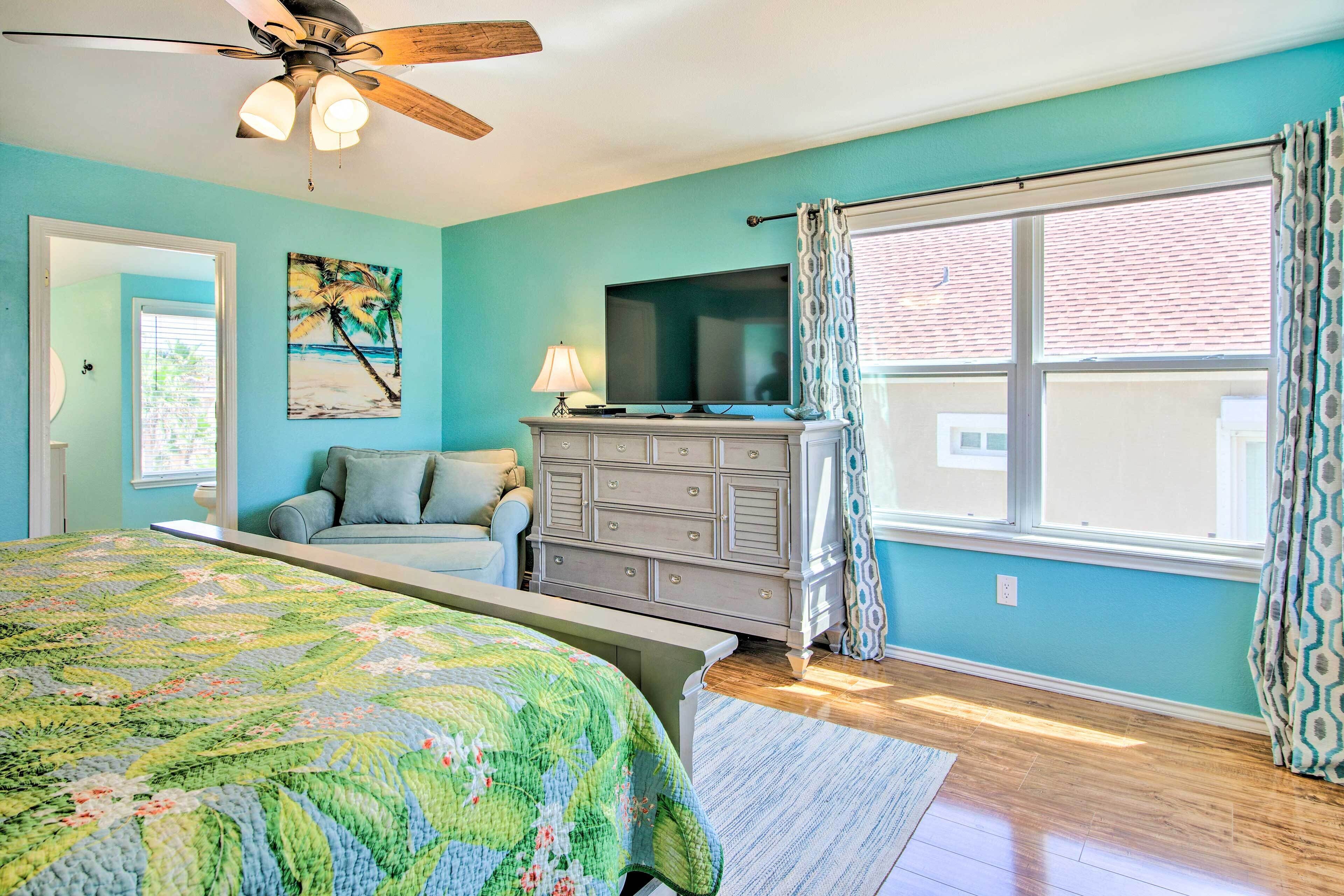 A bedroom with a bed, dresser, TV, and large window with curtains.