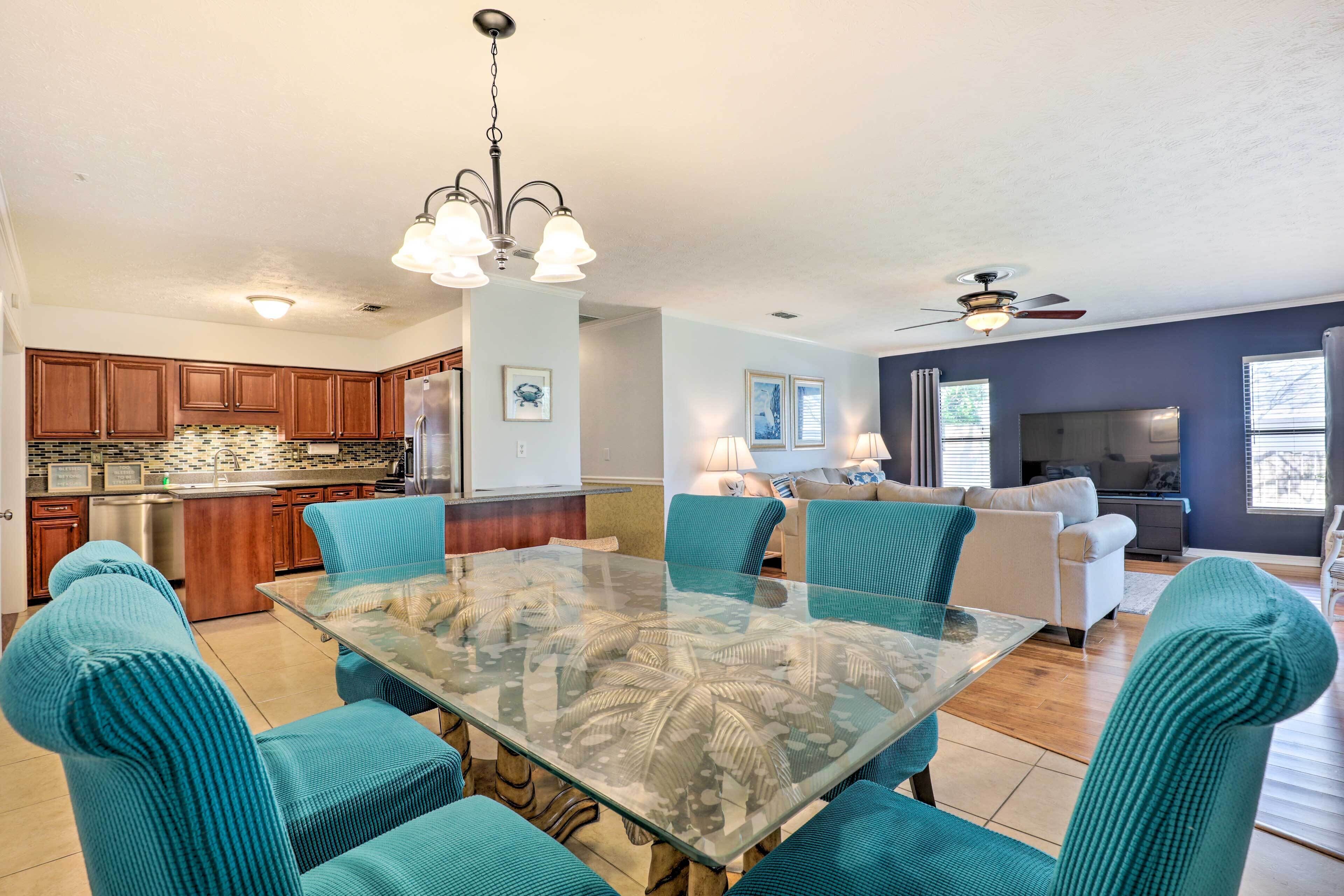 A spacious kitchen with wooden cabinets, a stainless steel refrigerator, and a glass dining table with teal chairs.