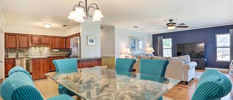 A spacious kitchen with wooden cabinets, a stainless steel refrigerator, and a glass dining table with teal chairs.