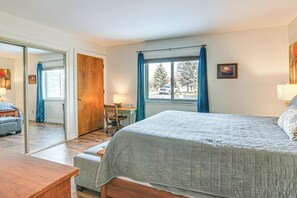 Ein Schlafzimmer mit Bett, Schreibtisch, Stuhl und einem fenster mit Vorhängen.