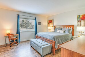 Ein Schlafzimmer mit einem hölzernen Bett, einem Schreibtisch mit Stuhl, einer Bank und einem Fenster mit Vorhängen.